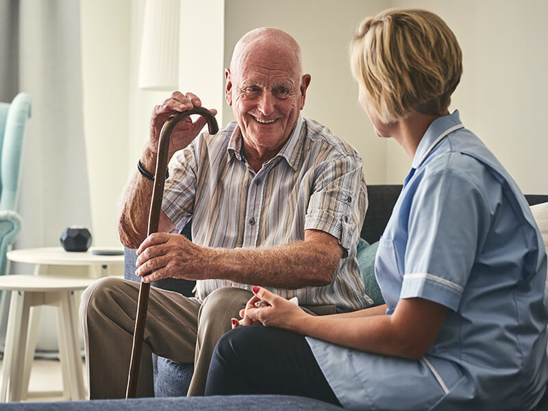 A carer speaking to an elderly man with a walking stick