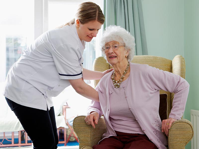 An elderly woman trying to stand up with support from a nurse