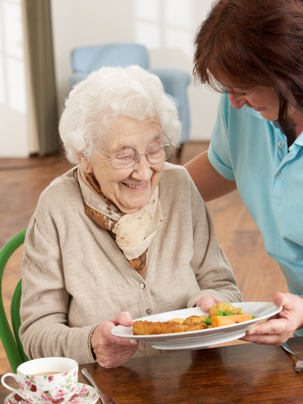Elderly woman and carer serving food