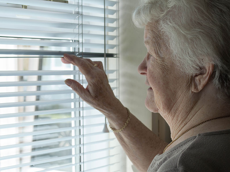 A senior woman looking through blinds