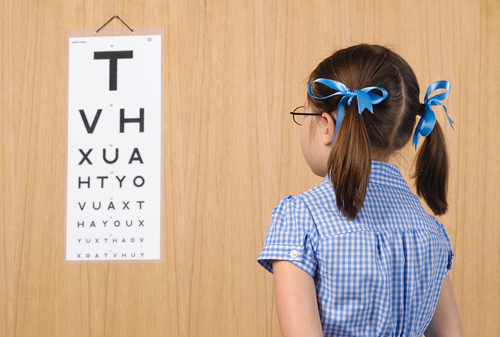Girl 5 7 taking eye test facing chart on wall rear view