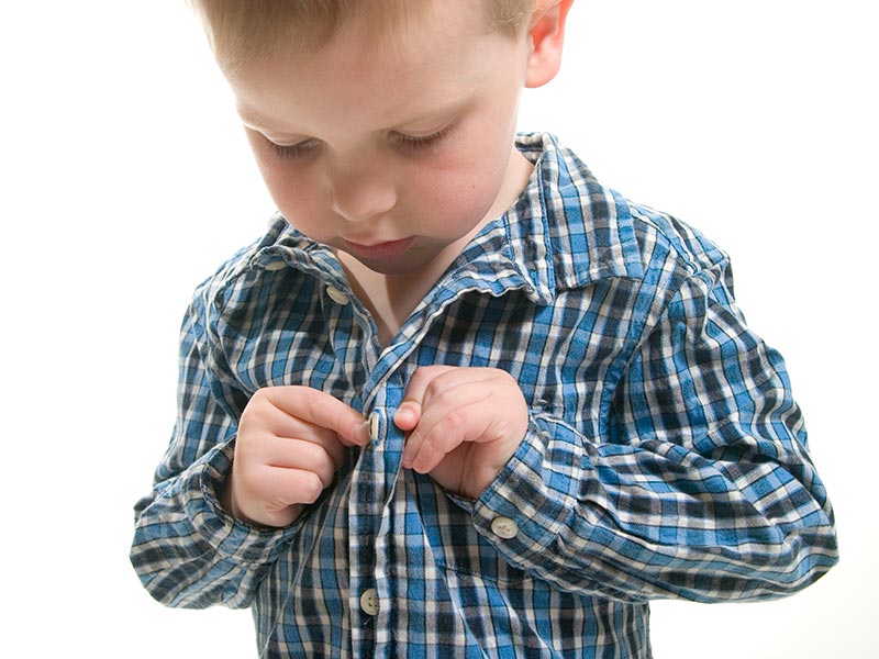 A young boy buttoning his own shirt