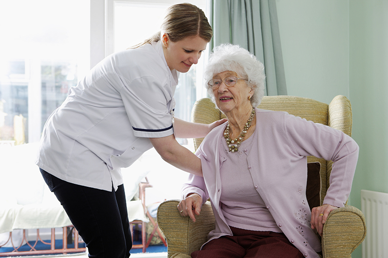 Elderly woman attempting to stand with help of a nurse