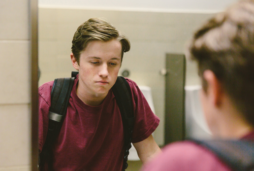 Teen looks at himself in the bathroom mirror