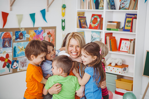 A nursery nurse being hugged by young children